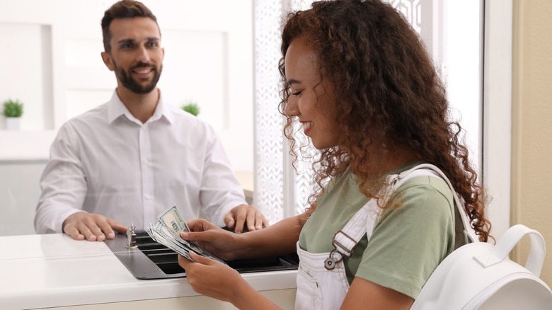Young woman counts money at bank counter