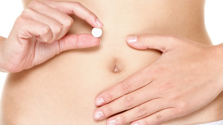 Woman holding pill near stomach