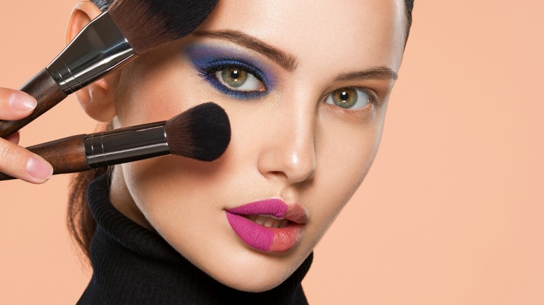 woman holding makeup brushes over face